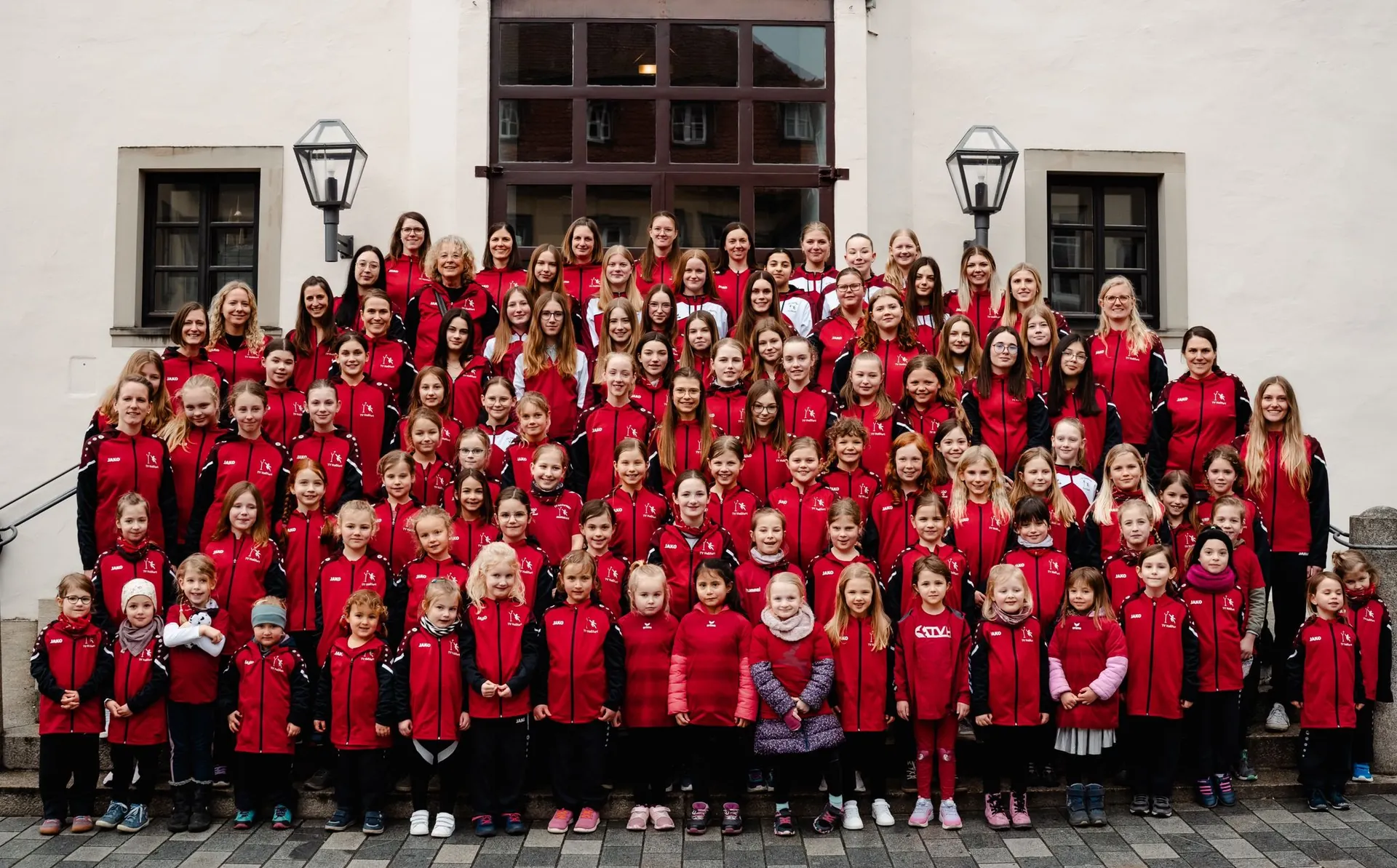 Gruppenfoto der Korbball-Abteilung in roten TV-Jacken auf einer Treppe