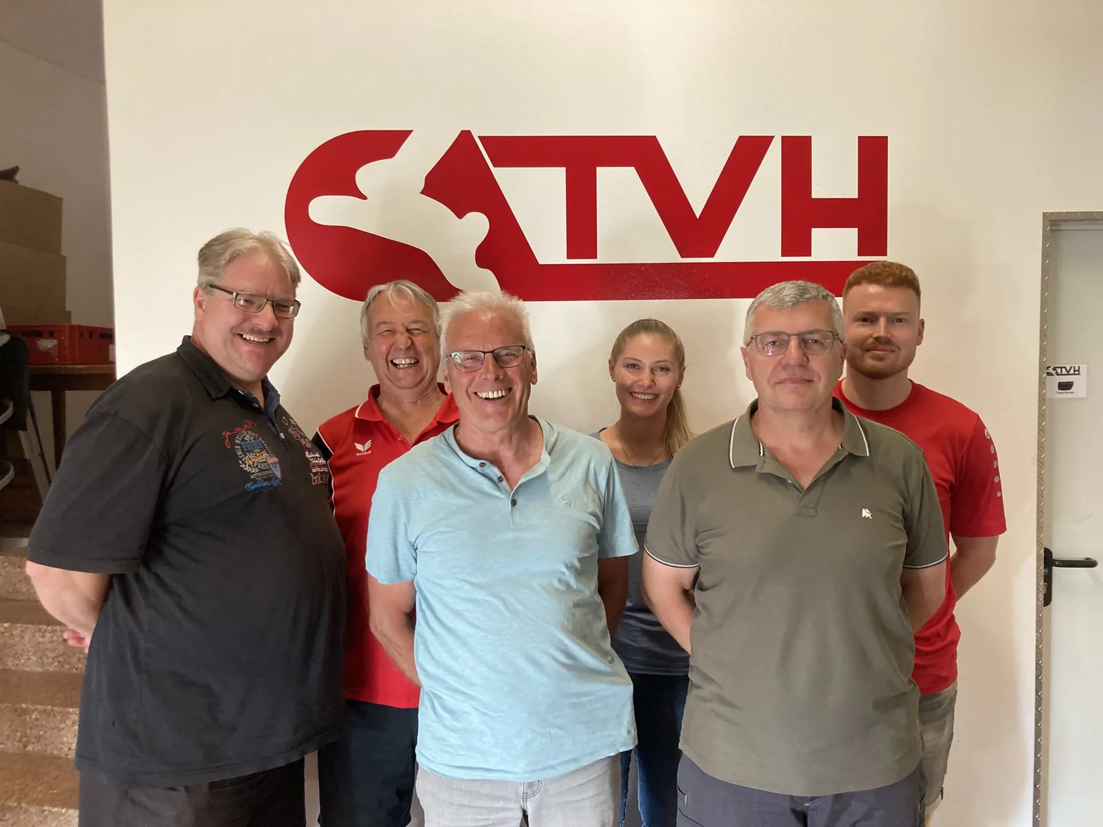 Die Vorstandschaft des TV Haßfurt vor dem TVH-Logo